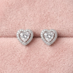Heart shaped silver halo stud earrings with sparkling crystals resting on a soft pink velvet background⁠