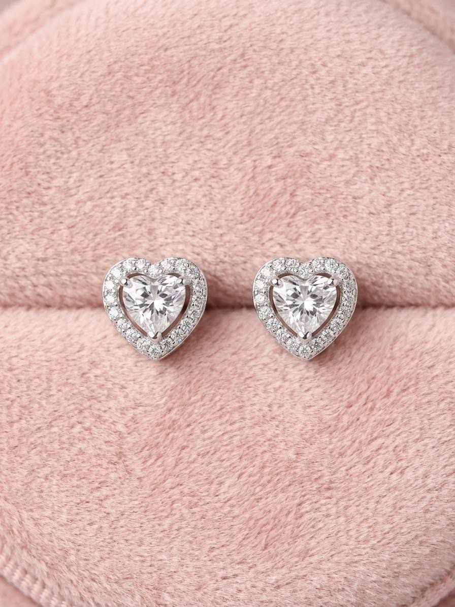 Heart Shaped Halo Stud Earrings Heart shaped silver halo stud earrings with sparkling crystals resting on a soft pink velvet background